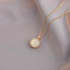 Gold necklace with a round pendant on a soft gray background