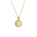 A gold chain necklace with a circular pendant featuring a central milky white stone surrounded by a halo of small clear stones, on a plain white background.