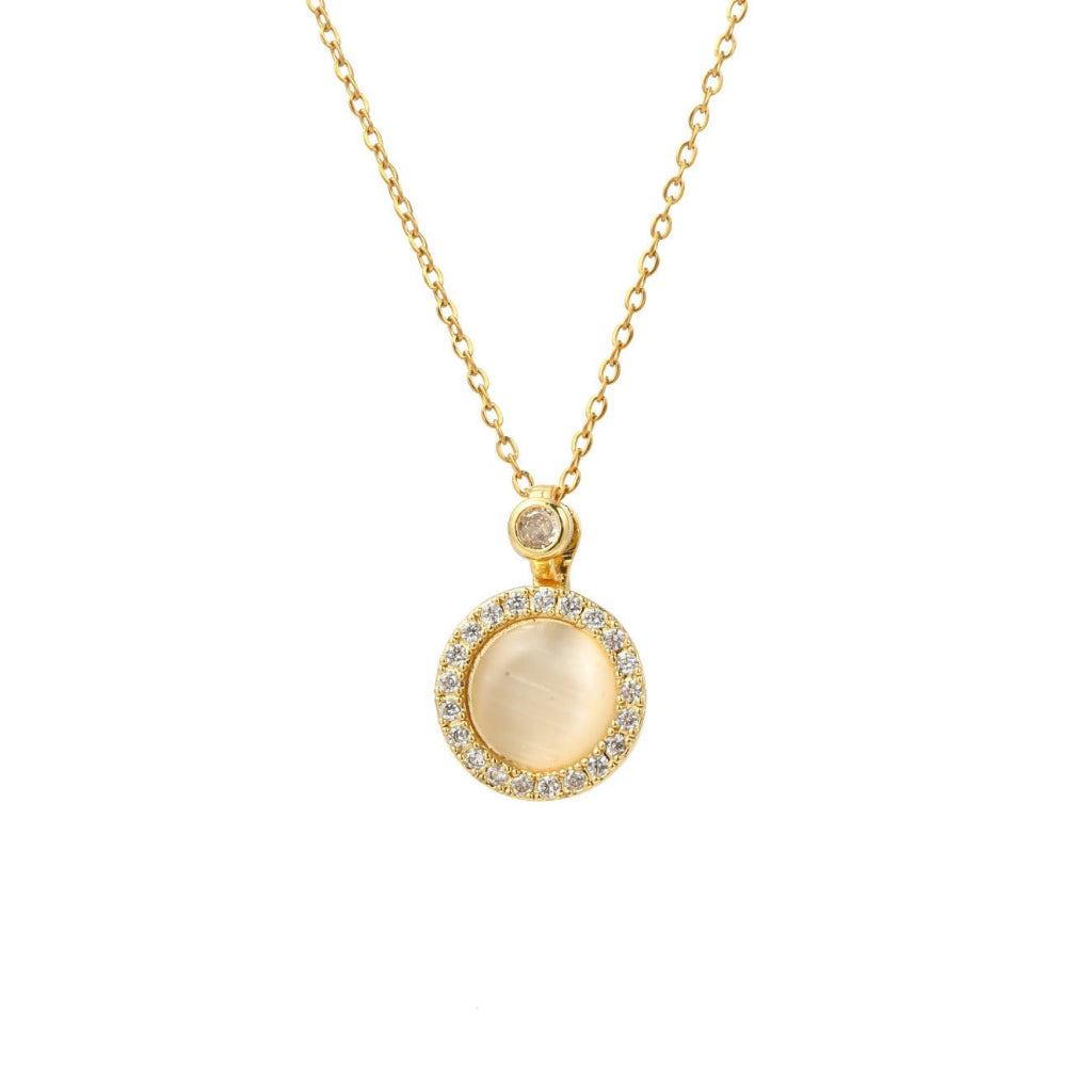 A gold chain necklace with a circular pendant featuring a central milky white stone surrounded by a halo of small clear stones, on a plain white background.