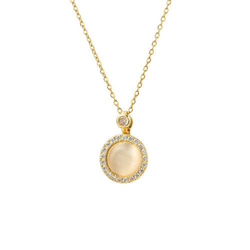 A gold chain necklace with a circular pendant featuring a central milky white stone surrounded by a halo of small clear stones, on a plain white background.