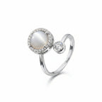 A silver ring featuring a large oval white pearl surrounded by a halo of small clear stones, with a separate round clear stone set on a polished silver band, shown on a white background.