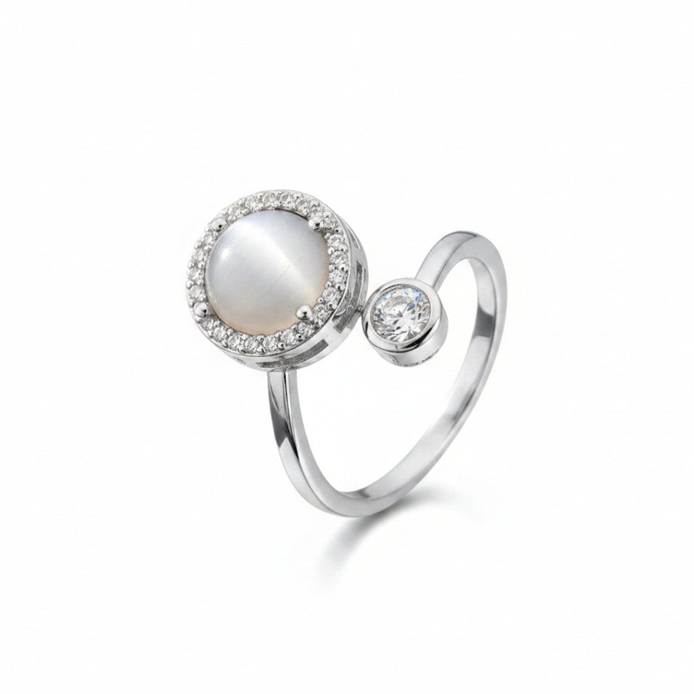 A silver ring featuring a large oval white pearl surrounded by a halo of small clear stones, with a separate round clear stone set on a polished silver band, shown on a white background.