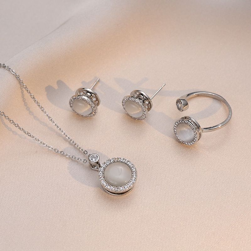 Silver jewelry set with necklace, earrings, and ring on a beige background