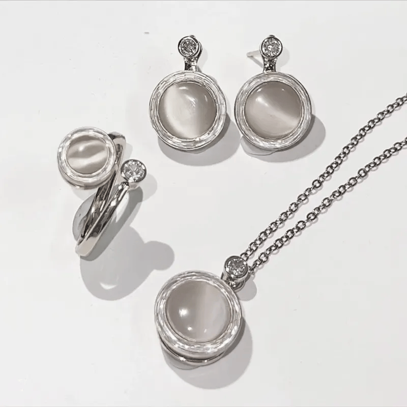 Silver jewelry set with pendant, ring, and earrings on a white background