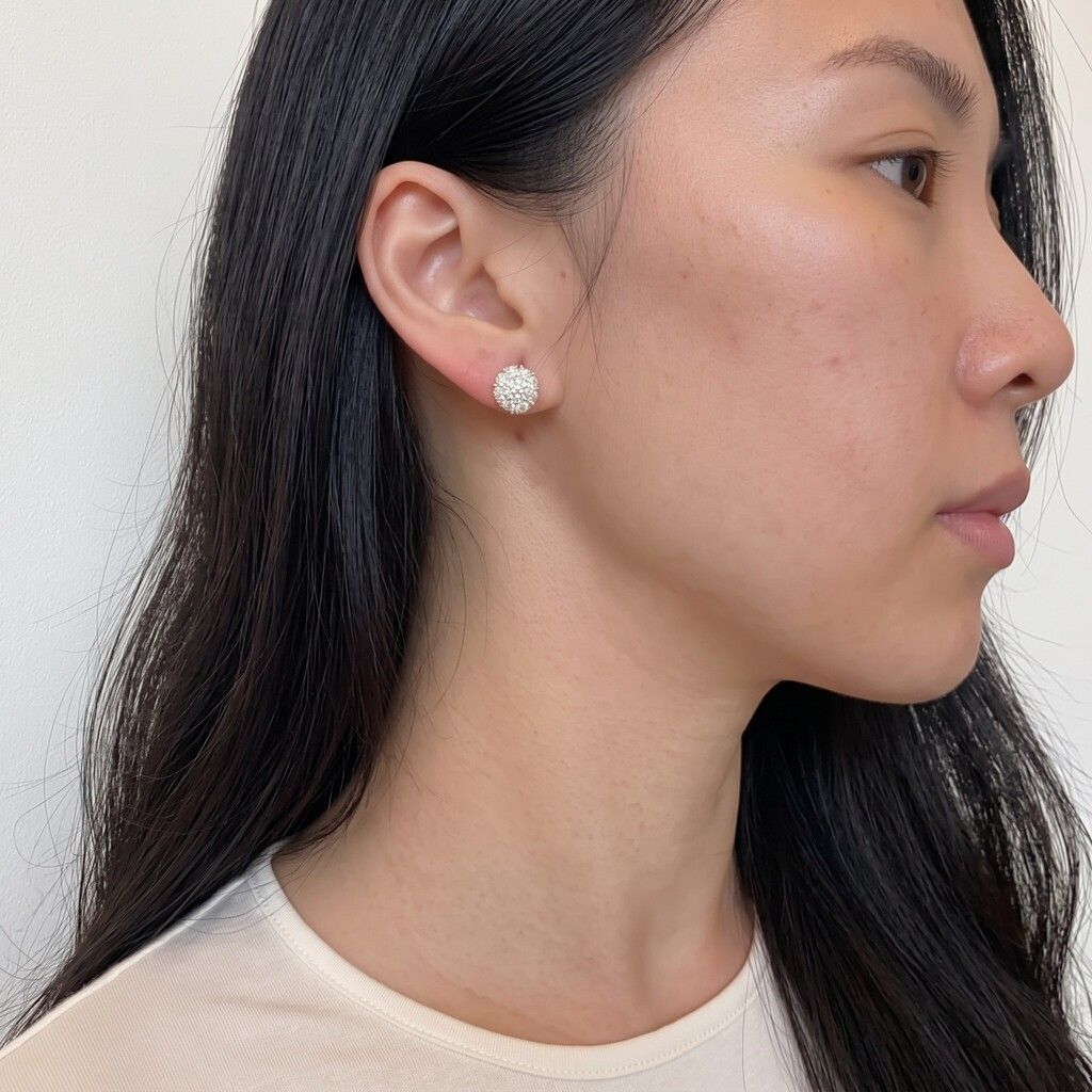 A close-up side profile of a woman wearing a small, round, textured silver stud earring on her earlobe.
