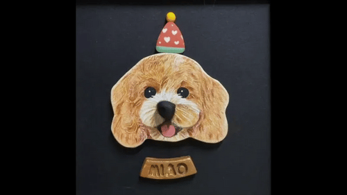 A custom pet portrait plaque featuring a detailed sculpted dog head with a small party hat and a name plate reading 'MIO' below, set against a dark background.