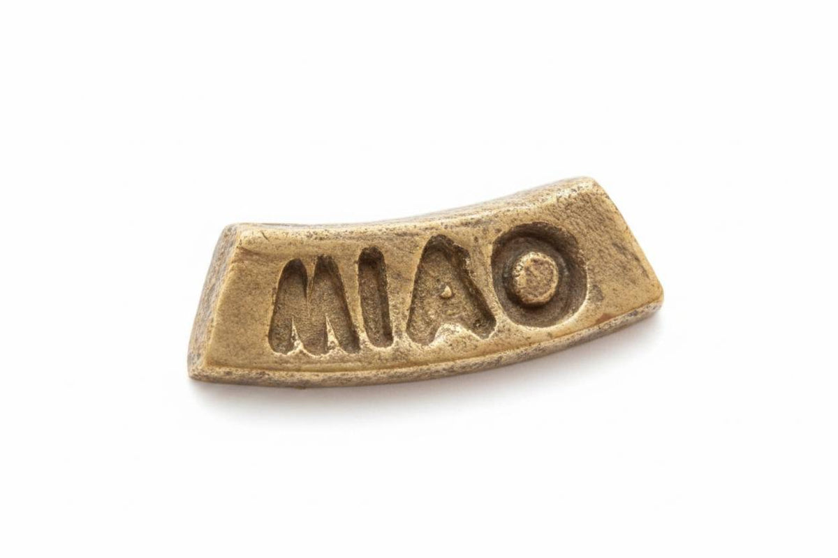A small curved metallic pin or charm with the word 'MIAO' cut out in the center, shown on a plain white background.