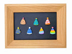 A square wooden frame containing a dark chalkboard-style center with eight small colorful cone-shaped ornaments or magnets arranged in two rows. The frame is light natural wood, and the ornaments feature various patterns including stripes, polka dots, leopard print, and rainbow stripes on a plain white background.