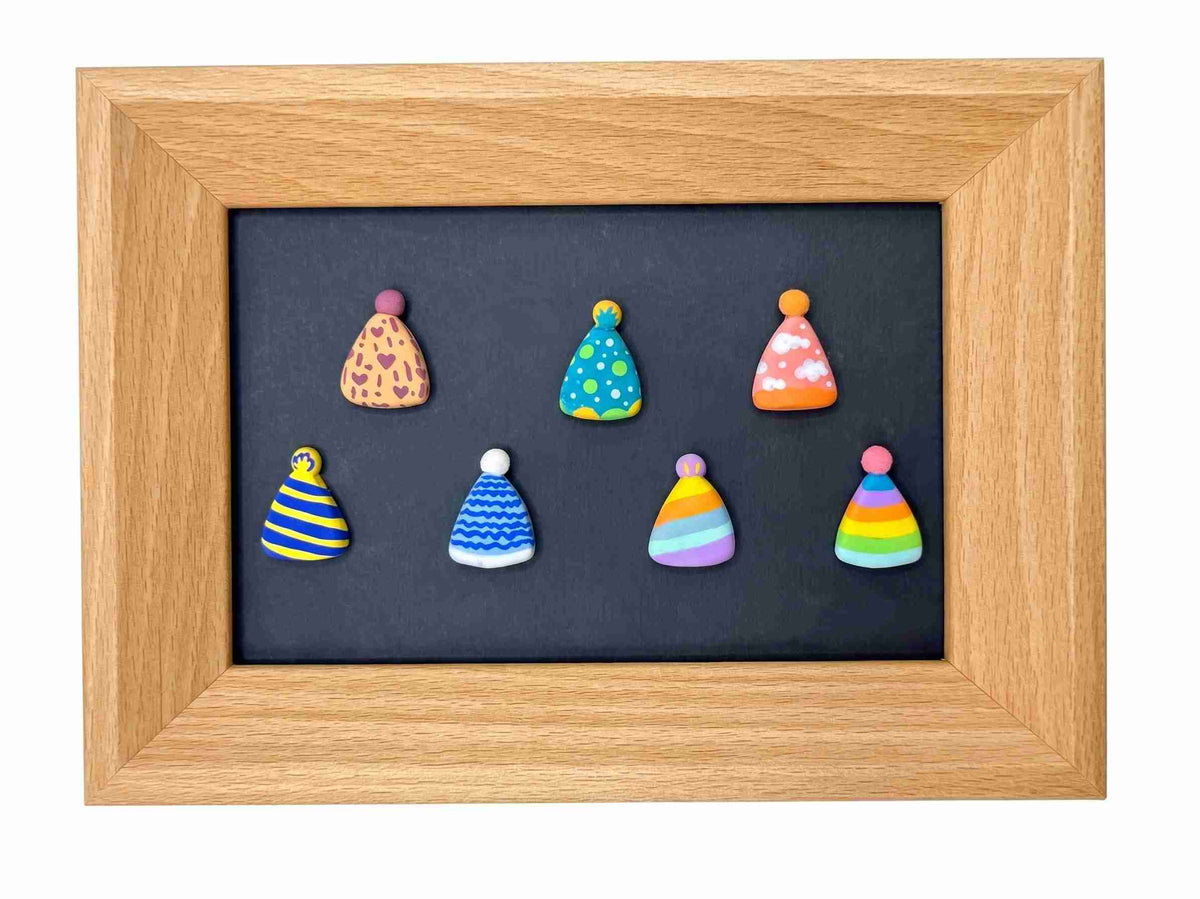 A square wooden frame containing a dark chalkboard-style center with eight small colorful cone-shaped ornaments or magnets arranged in two rows. The frame is light natural wood, and the ornaments feature various patterns including stripes, polka dots, leopard print, and rainbow stripes on a plain white background.