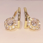 A pair of gold hoop earrings with large, textured clear crystal or diamond flower-shaped studs, shown against a plain light beige background.