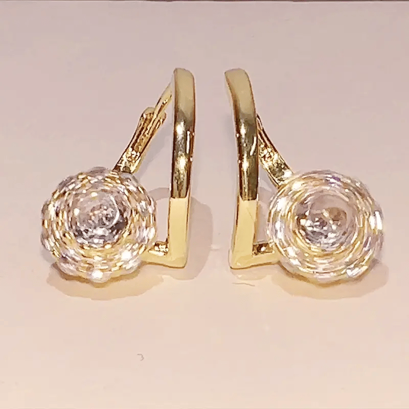 A pair of gold hoop earrings with large, textured clear crystal or diamond flower-shaped studs, shown against a plain light beige background.