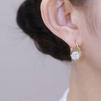 Close-up of an ear wearing a gold hoop earring with a clear gemstone on a neutral background