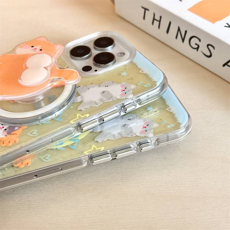 A clear phone case with a pastel cat illustration and a built-in pop socket, shown on a light wood surface next to a white book.