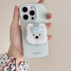A hand holds a phone case decorated with a cute white polar bear character and a small blue bow. The case itself is a very pale mint green with subtle speckles, and the phone inside is visible.