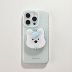 A clear speckled phone case with a 3D white bear pop socket featuring a light blue bow, shown on a light gray background.