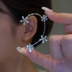 Close-up of a person wearing a silver earring with floral designs and holding another similar earring.