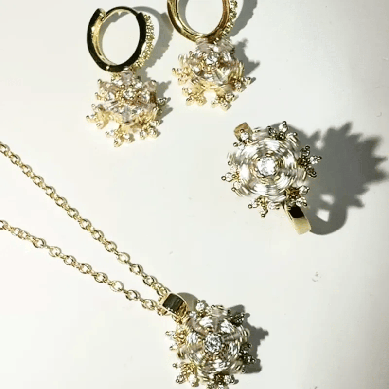 Gold jewelry set featuring a necklace, ring, and hoop earrings with matching clear crystal starburst flower pendants, displayed on a white surface.