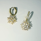 A pair of gold hoop earrings with dangling snowflake and spiral flower charms, embellished with clear rhinestones, shown on a plain white surface.