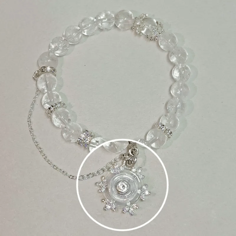 A clear crystal beaded bracelet with silver-toned chain and rhinestone accents, featuring a circular clear crystal pendant with a central clear stone, shown on a light neutral background.