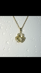 A gold-tone rose-shaped pendant necklace with a matching chain, displayed against a white textured surface with water droplets.