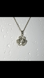 A silver-tone flower pendant necklace with a clear central gemstone, hanging from a matching chain against a white background with water droplets.