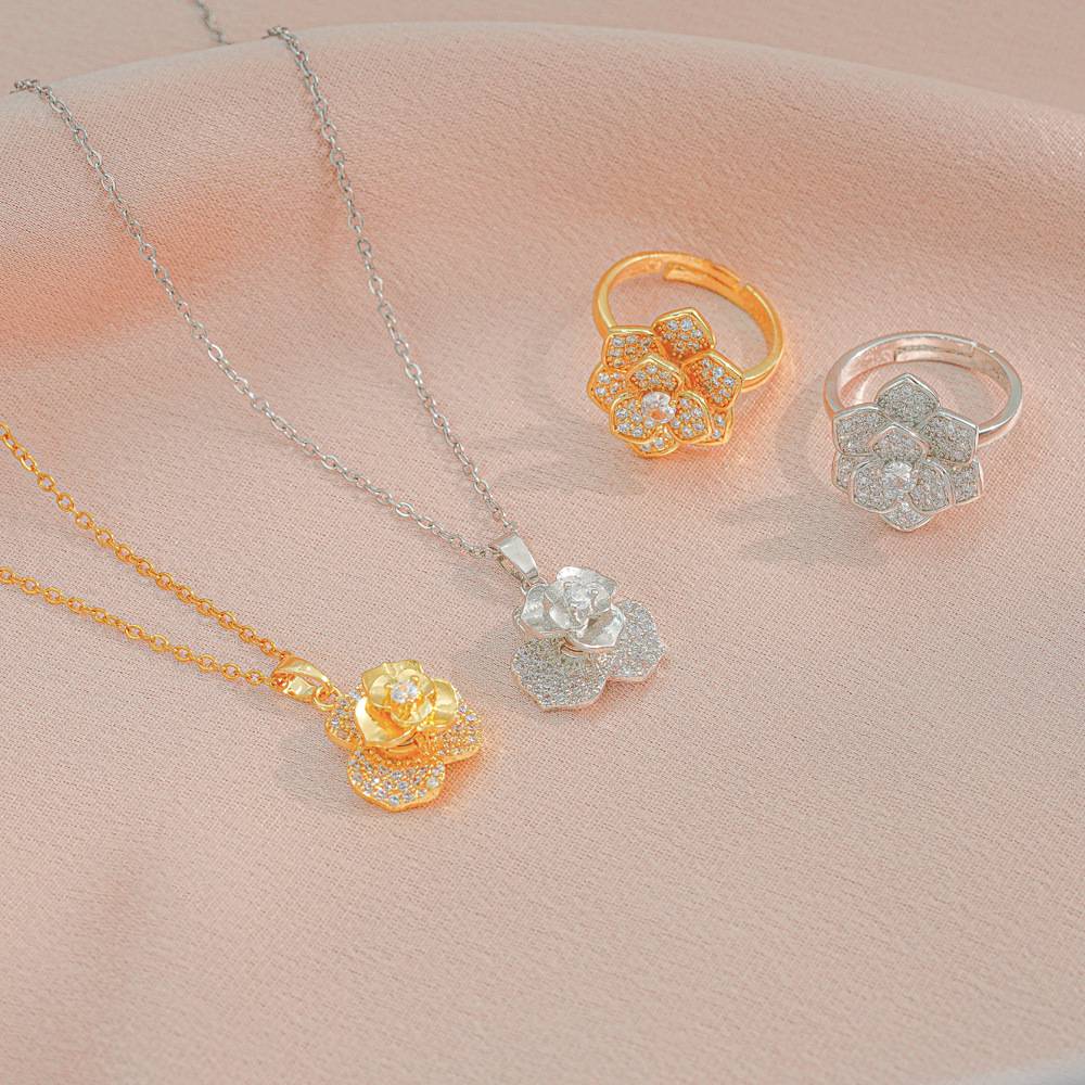 Jewelry set with floral pendants and rings on a soft pink fabric background