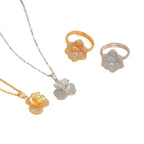 Four jewelry pieces on a plain white background: two flower-shaped pendant necklaces in yellow gold and white gold/silver tones, and two matching flower-shaped rings in yellow gold and rose gold tones. The stones are clear and do not contribute a color per the schema.