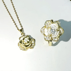 A gold rose-shaped pendant necklace and matching rose ring set, both adorned with clear rhinestones, displayed on a white background.