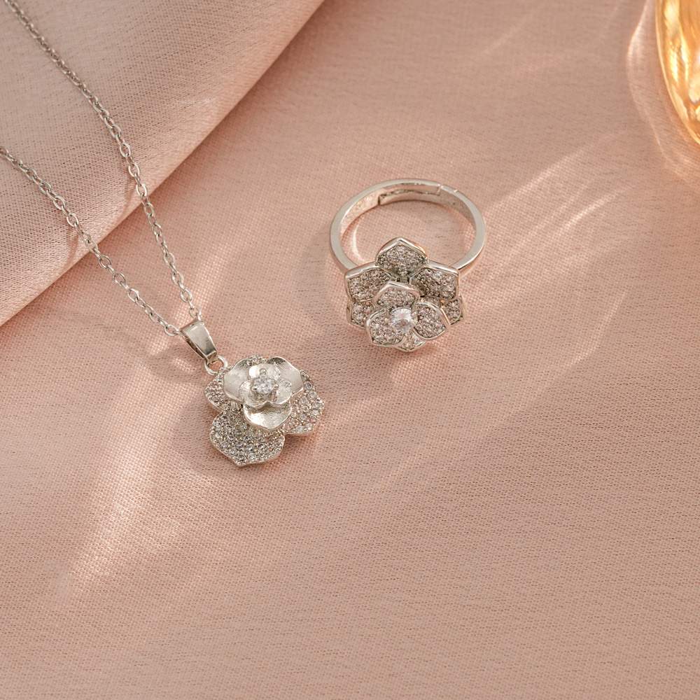 Silver flower-shaped necklace and ring on a pink fabric background