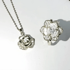 Silver-tone rose-shaped pendant necklace and matching ring set, both adorned with clear rhinestones, displayed on a white background.
