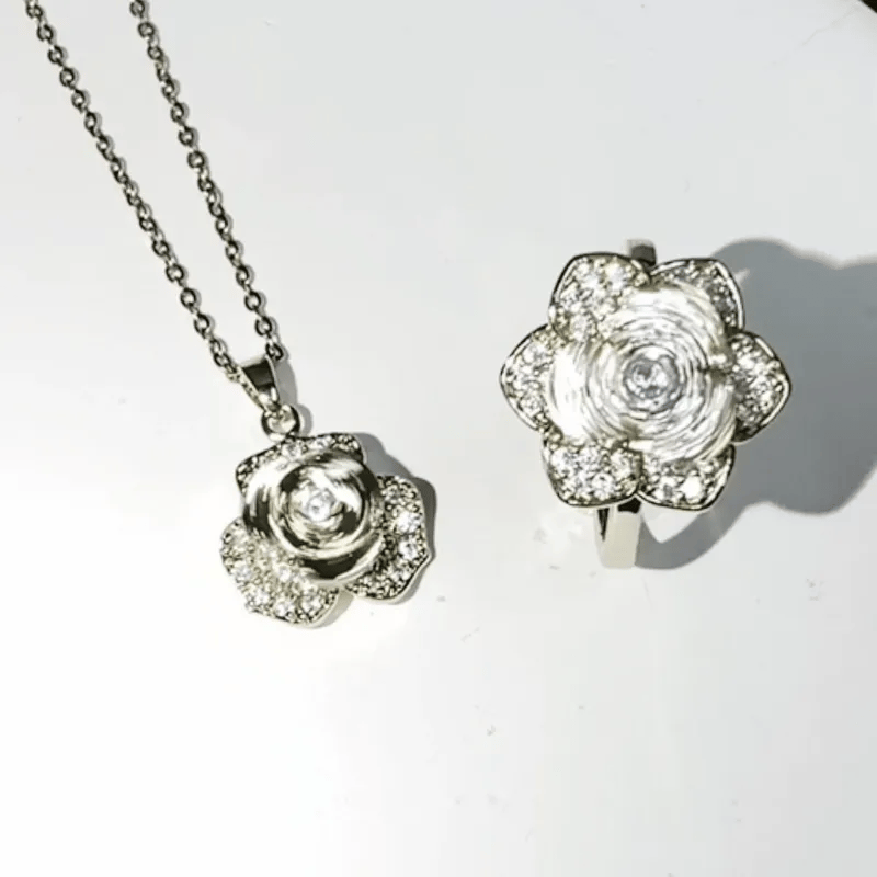 Silver-tone rose-shaped pendant necklace and matching ring set, both adorned with clear rhinestones, displayed on a white background.