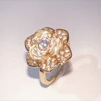 A gold flower-shaped ring with a central clear gemstone and smaller pavé-set stones, photographed on a plain light background.