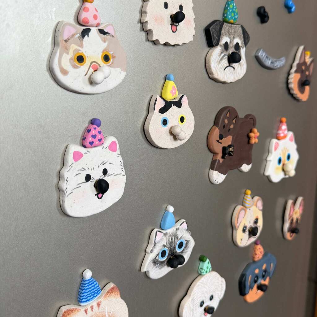 A set of colorful dog-shaped refrigerator magnets with party hats, displayed on a gray metal refrigerator door.