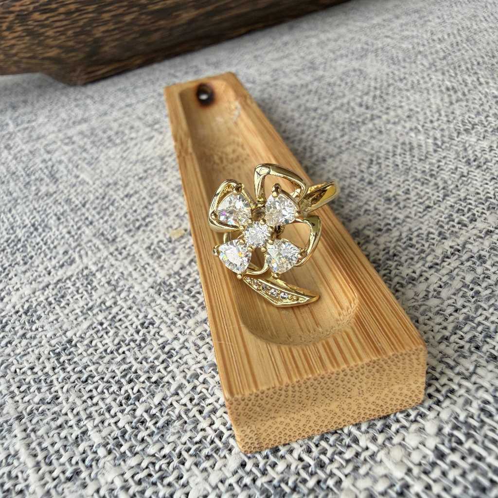 A gold flower-shaped ring with clear gemstones sits in a small wooden tray on a textured gray fabric surface.