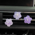 Three lavender purple flower-shaped car air fresheners clipped onto a car dashboard air vent.