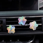 Three pastel iridescent flower-shaped air fresheners attached to a car's air vent grilles.