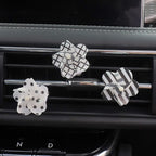 Three decorative car air freshener flowers with black and white patterns, clipped to the air vents of a car dashboard.