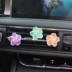 Three flower-shaped car air fresheners in purple, mint green, and peach, attached to a car's air conditioning vent.