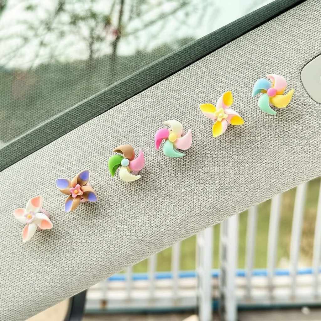 Five pastel flower-shaped car accessory clips attached to a light gray sun visor, with a blurred outdoor background visible through the window.