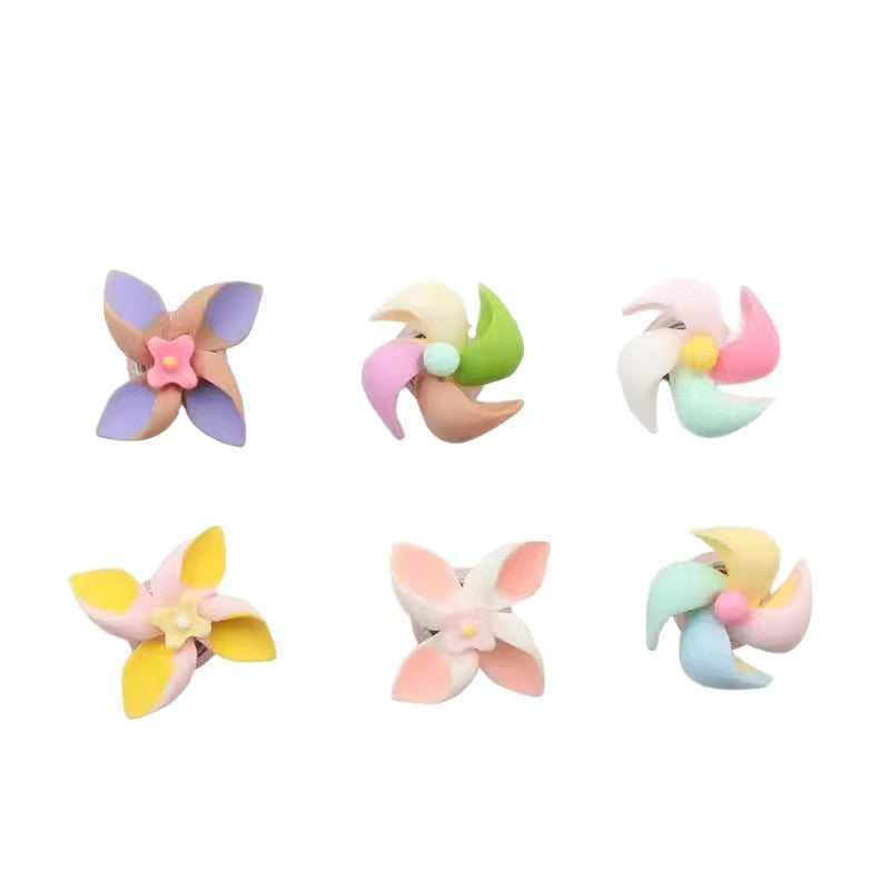 Six pastel pinwheel-shaped accessories arranged in two rows on a plain white background. The pinwheels feature soft pastel colors including lavender, pink, green, yellow, peach, and light blue.
