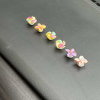 Five small pastel flower-shaped accessories arranged diagonally on a dark gray textured surface.