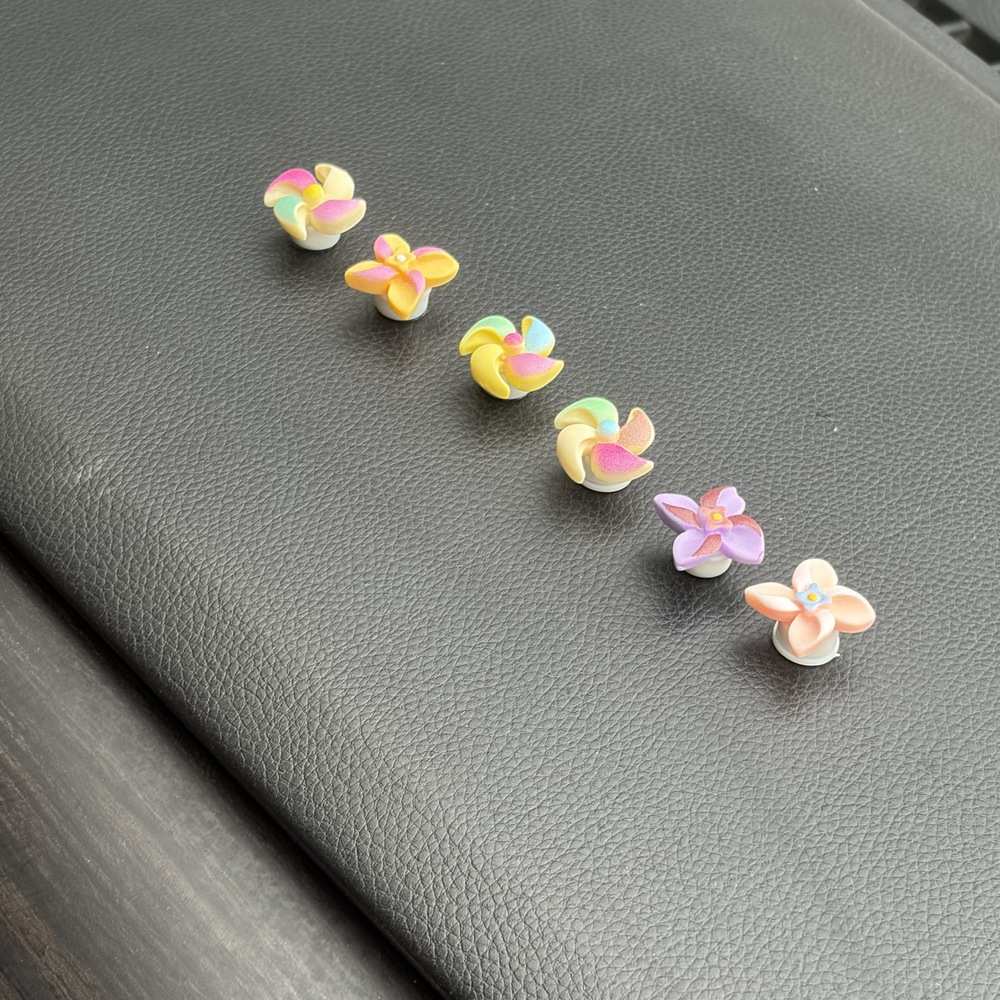 Five small pastel flower-shaped accessories arranged diagonally on a dark gray textured surface.