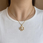A gold cross pendant necklace with a central white pearl and small clear stones, worn on a model's neck over a white t-shirt.