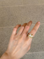 A gold ring with a large clear gemstone cluster, worn on a person's finger against a gray tiled background.