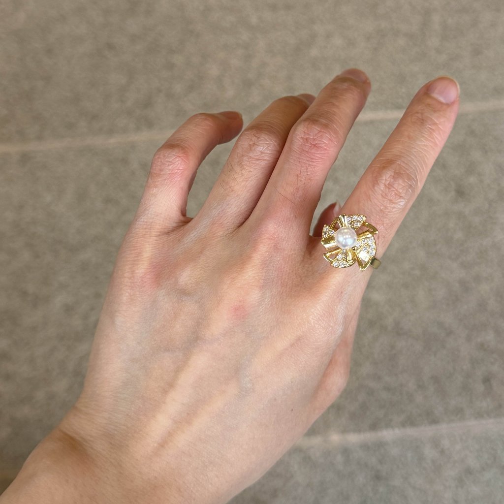A gold ring with a large clear floral cluster gemstone worn on a person's finger, shown against a neutral gray tiled background.