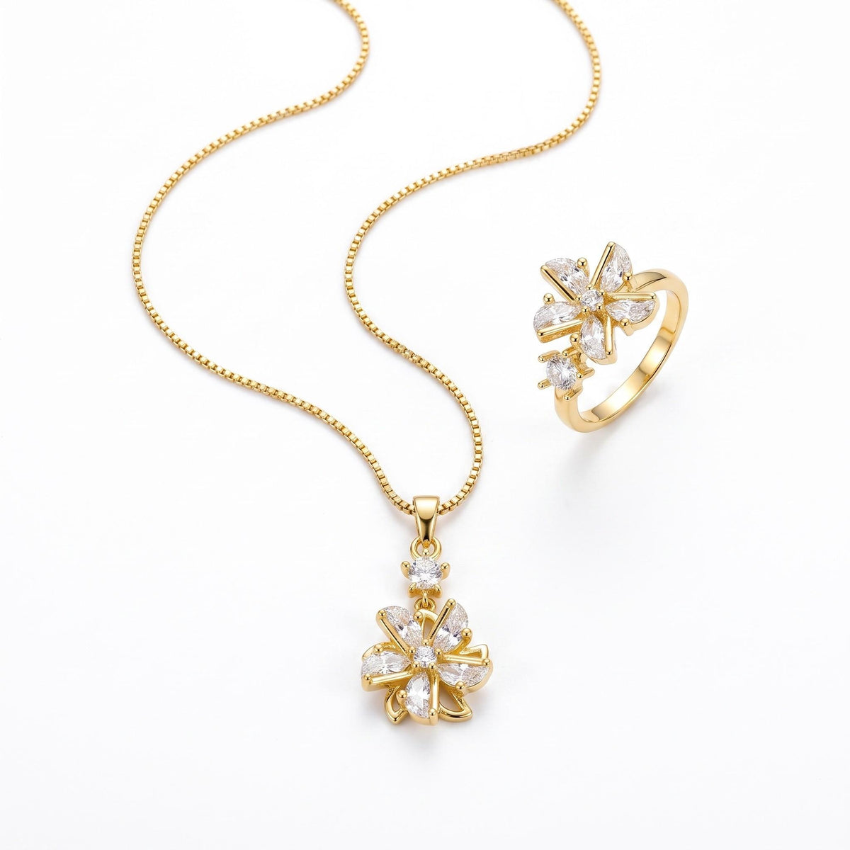 A gold jewelry set featuring a delicate chain necklace and a matching ring, both adorned with clear, sparkling flower-shaped stones in a gold setting, displayed on a clean white background.