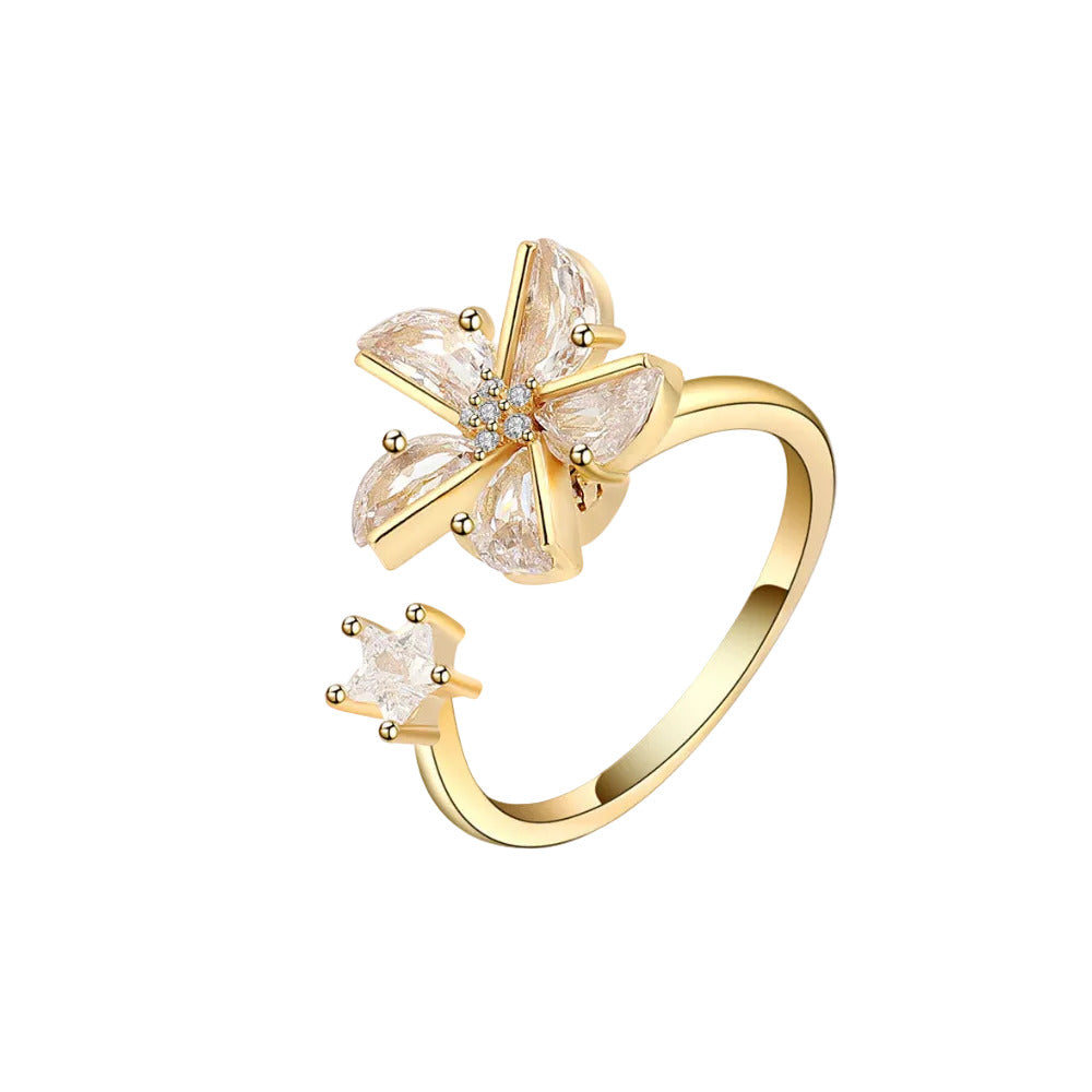 A gold ring featuring a flower-shaped setting with clear gemstones and a small crown-shaped clear gemstone on the band, shown on a plain white background.