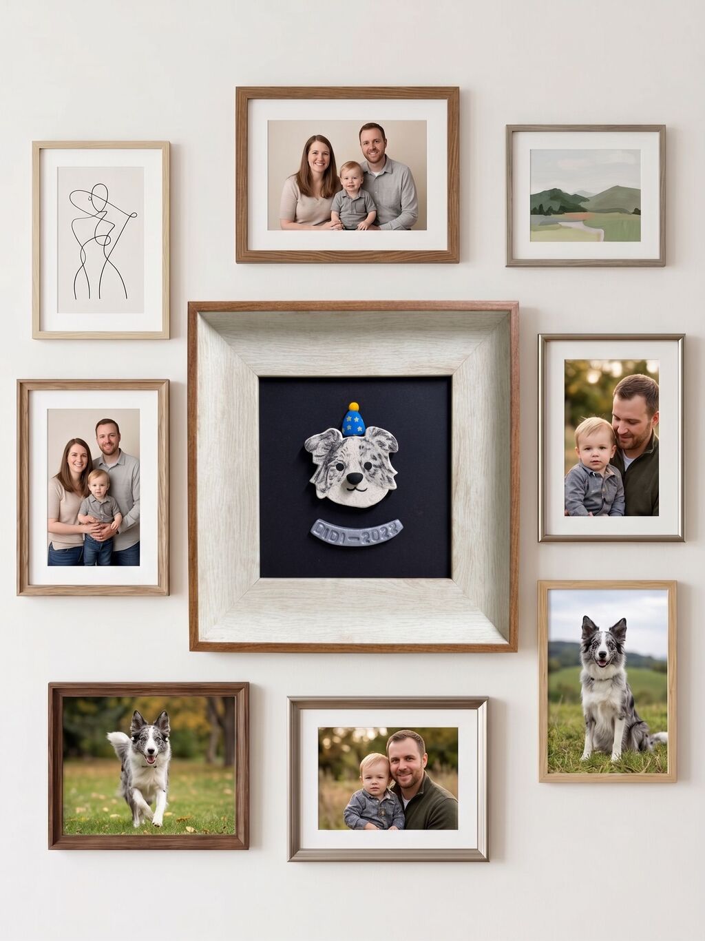 A styled gallery wall arrangement of multiple framed photographs and a central framed emblem. The collection includes family portraits, a minimalist line drawing, a landscape photo, and a dog portrait, all housed in light wood, white, and dark brown frames against a warm off-white wall.